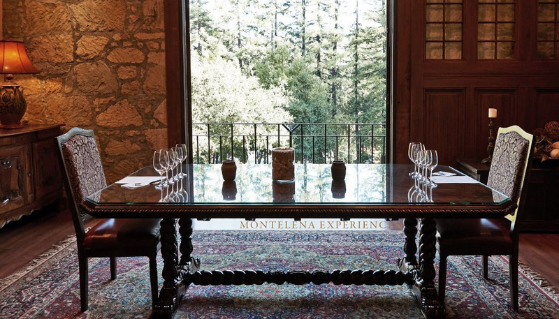 Two chairs sit opposite each other at a long, ornate tasting table in a dark, luxurious room with stone walls | Best Wineries in Calistoga