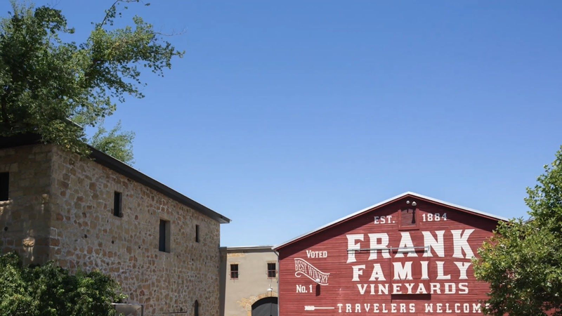 The words "Frank Family Vineyards: Travelers Welcome" are written in white across a red building under a bright blue sky | Best Wineries in Calistoga
