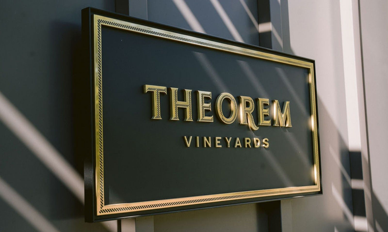 A black plaque reading "Theorem Vineyards" in gold lettering hangs on a wall | Best Wineries in Calistoga