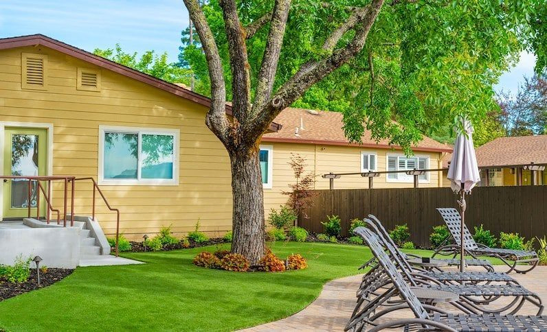 A yellow building is pictured, with rich green grass and an array of iron lawn chairs nearby for guests to relax in the sun | Best Calistoga Hotels