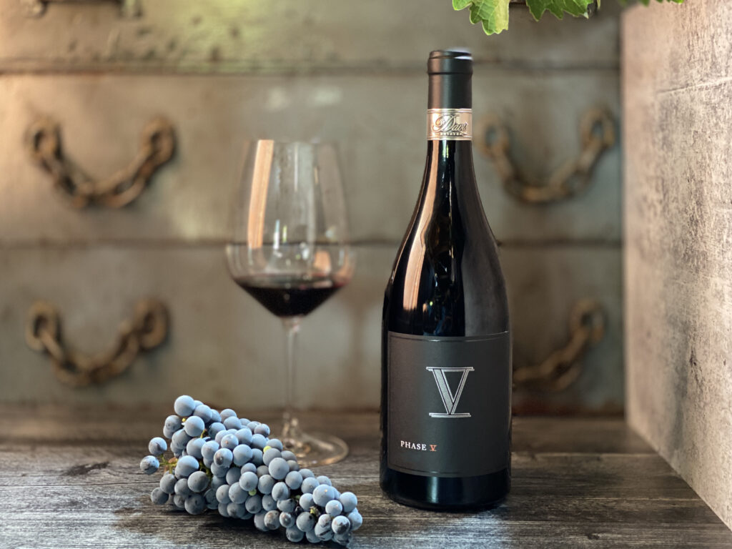 Phase V wine bottle with glass and grapes on table