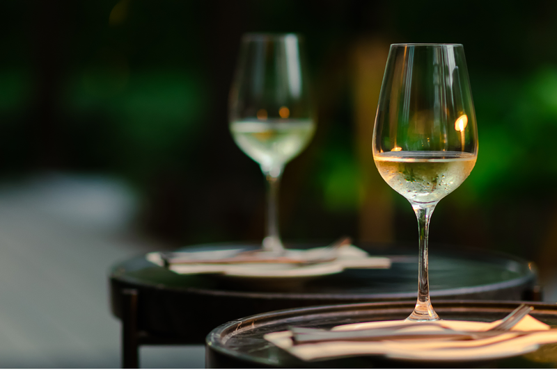 Two wine glasses with white wine on outdoor tables at dusk.