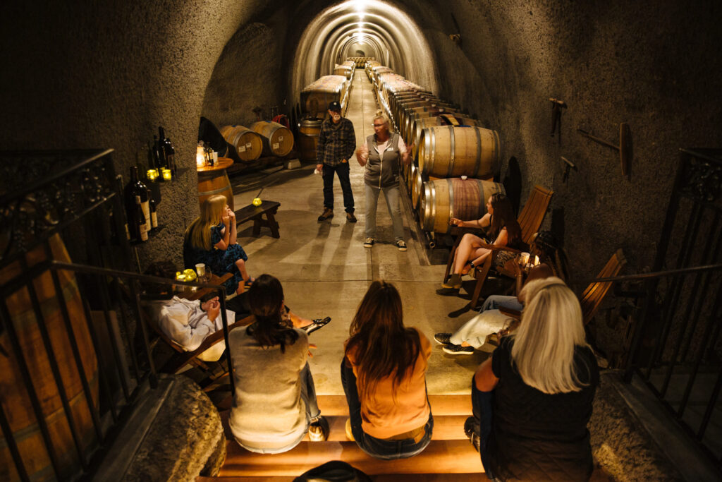 Wine cave tour with group seated near aging barrels