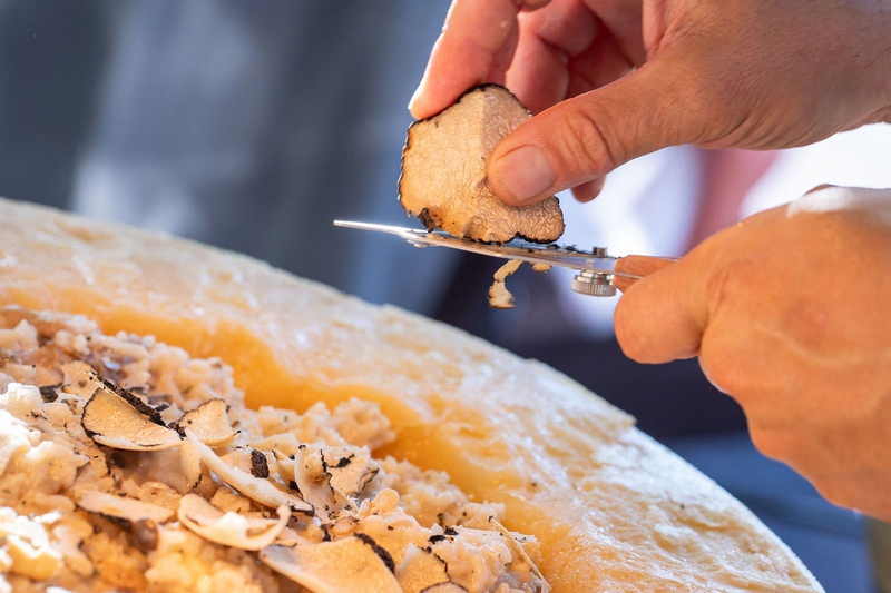 Shaving black truffle over creamy risotto in cheese wheel