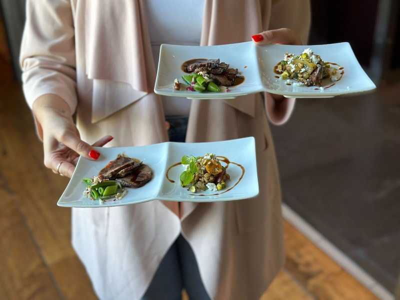 Person holding three gourmet tasting plates of assorted dishes