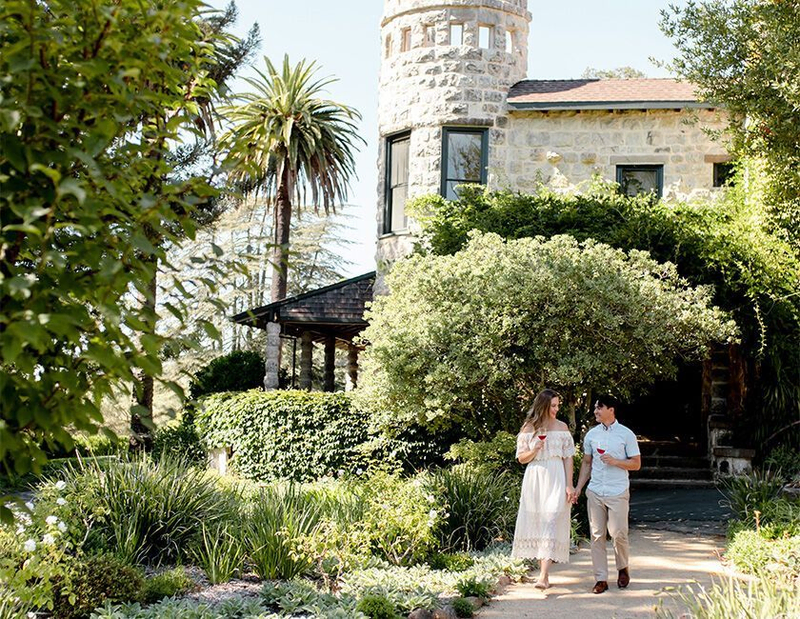 Couple walking by stone winery with gardens and tower