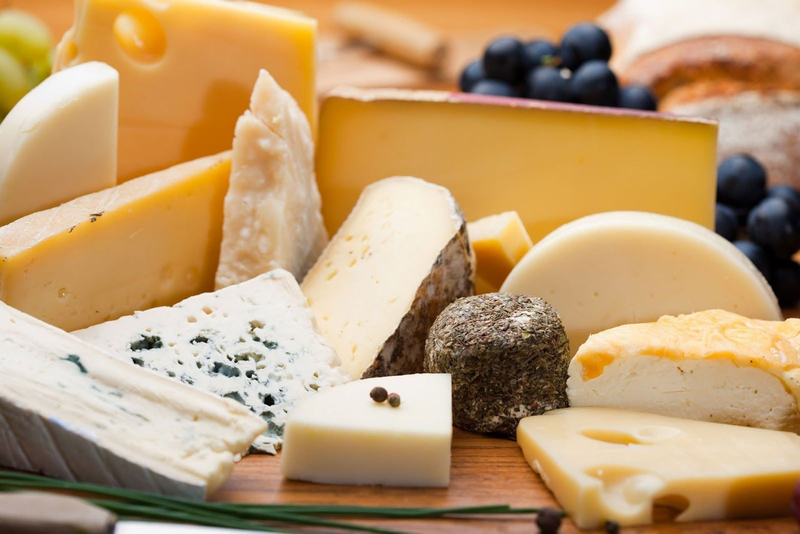 Assorted gourmet cheeses on a wooden board with grapes