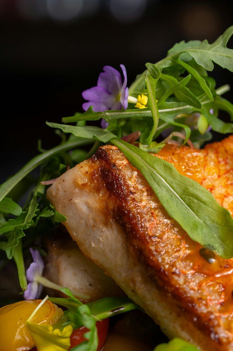 Close-up of gourmet fish dish with greens and flowers