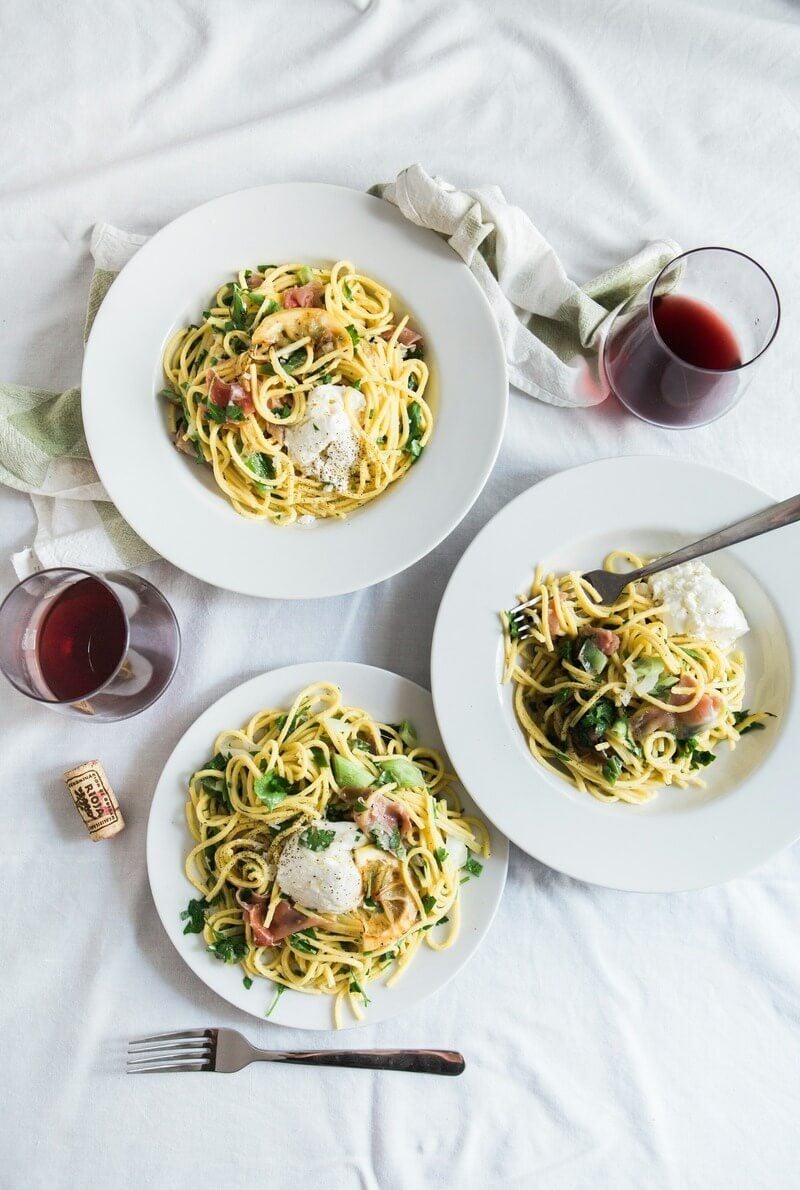Three plates of pasta with red wine on white tablecloth